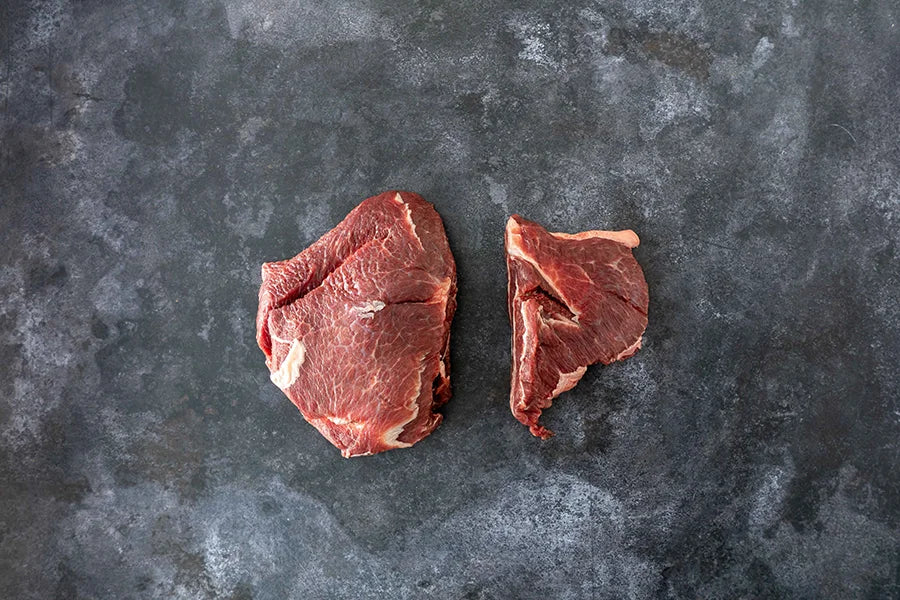 two raw beef cheeks sitting on dark marble kitchen top