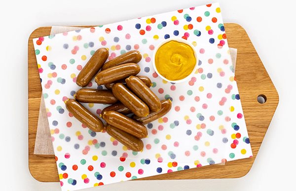 junior sausages on polka dot paper, on chopping board with mustard